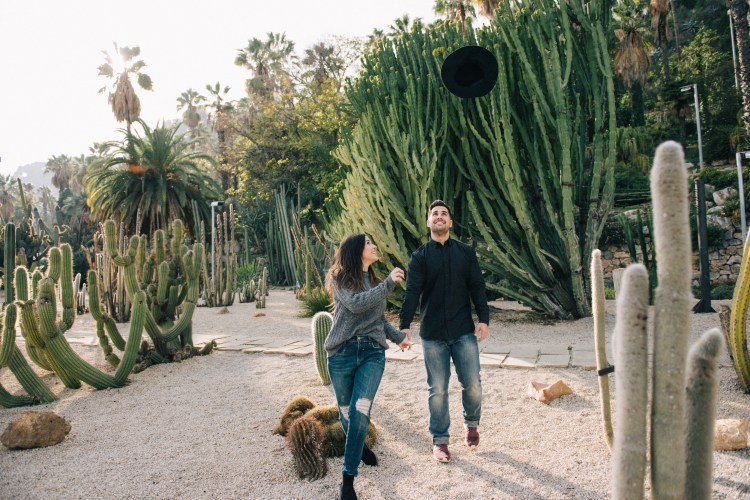 man and woman attracted to each other throwing hat up in the air in a dessert with cacti
